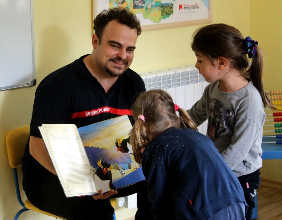Никола Райков чете с деца, които разглеждат разтворената книга